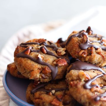 Banana, Date and Pecan Collagen Cookies drizzled with chocolate and piled high on a plate