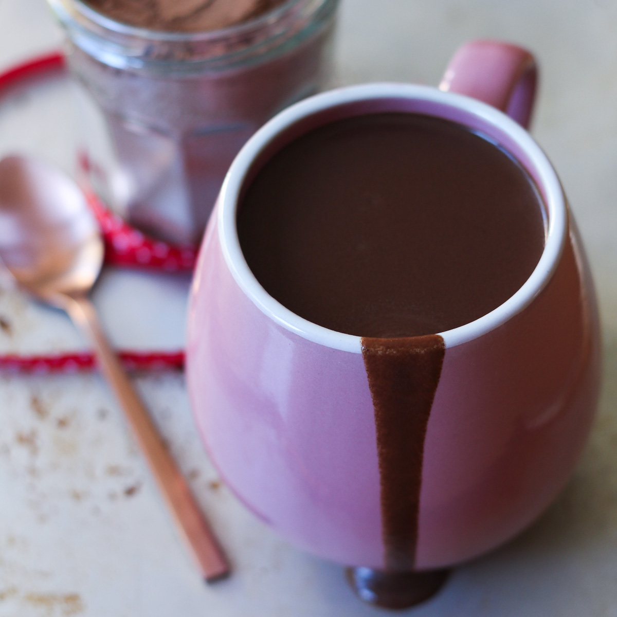 Close up image of hot chocolate in an oversized pink mug, with a drizzle down the side.