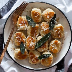 Ricotta gnocchi plated and garnished with crispy sage leaves and fresh grated parmesan